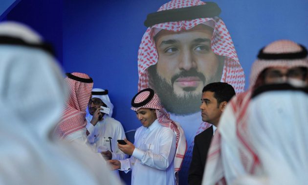 Saudi men chat in front of a poster of Saudi Crown Prince Mohammed bin Salman