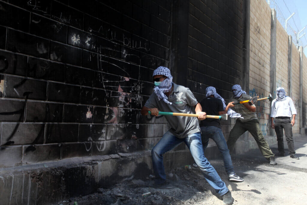 Palestinians youth use sledge hammers to knock holes through part of a wall