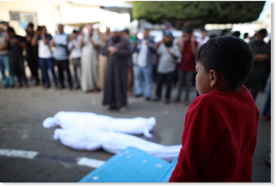 A Palestinian child looks at the bodies of martyrs.
